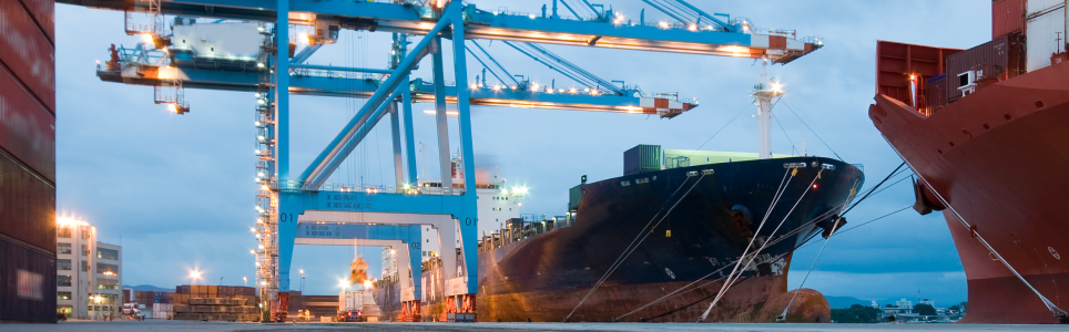 Rain clouds in the sky. Container terminal. Blue cranes. Container ship reflected in large puddle. Container stack on the left.