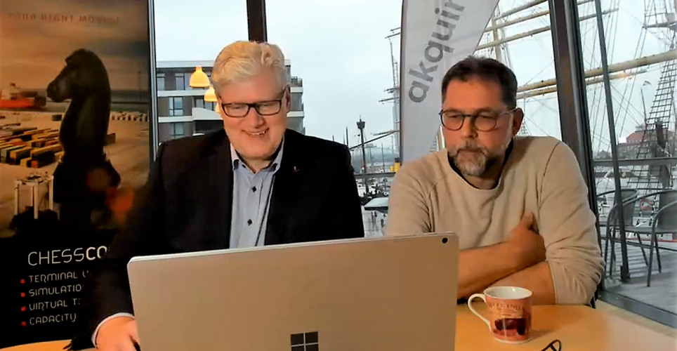 Oliver Jelsch and Horst-Dieter Kassel at the CHESSCON Conference 2022 in their office in Bremerhaven. In the background a banner of CHESSCON and AKQUINET. Both sit in front of the computer and smile at the conference guests.