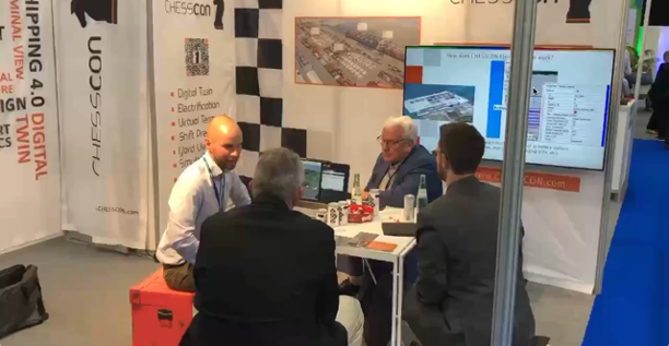 Port colleagues and customers sit around a table at the stand and chat animatedly. The picture shows the lively atmosphere at the Akquinet Port Consulting stand, where the interest in CHESSCON solutions is clear.