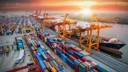 Bird's eye view of a container port with anchored ships. In the background the sun is setting.