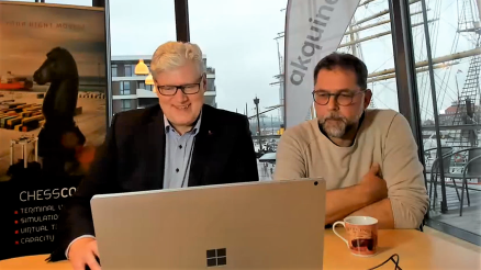 Oliver Jelsch and Horst-Dieter Kassel at the CHESSCON Conference 2022 in their office in Bremerhaven. In the background a banner of CHESSCON and AKQUINET. Both sit in front of the computer and smile at the conference guests.
