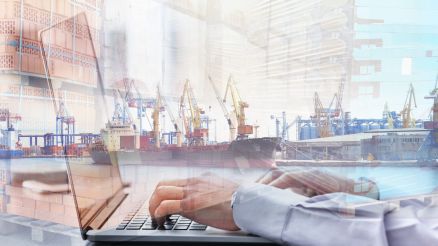 Person writing on a PC. A port terminal is visible in the background in a blur.